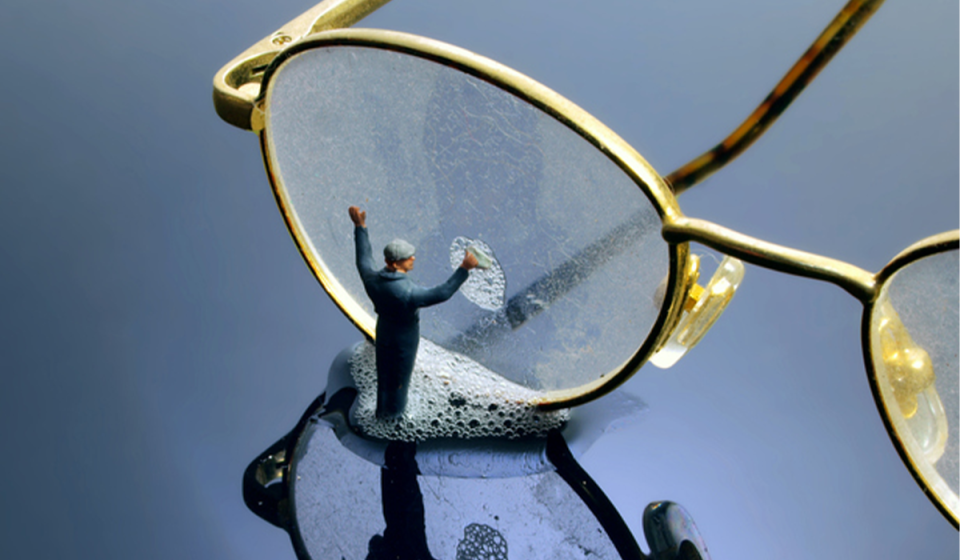 small man cleaning a pair of oversized glasses