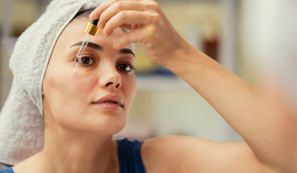 woman using oil dropper on face in the mirror