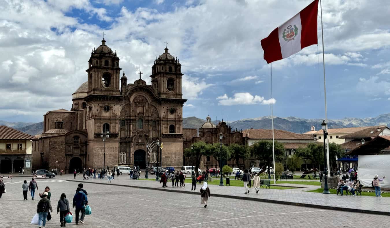 A sunny day in Peru with a huge flag waving in the breeze and historic buildings nearby