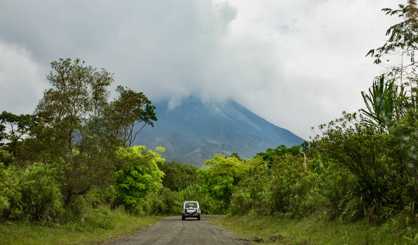 A car driving on an earthy road towards a cloudy volcano in Costa Rica