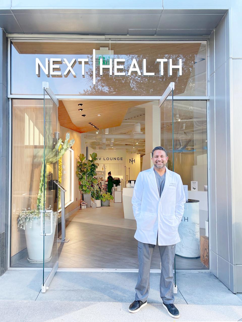 Darshan Shah is in a white laboratory coat, standing in front of his clinic, which reads "Next health."