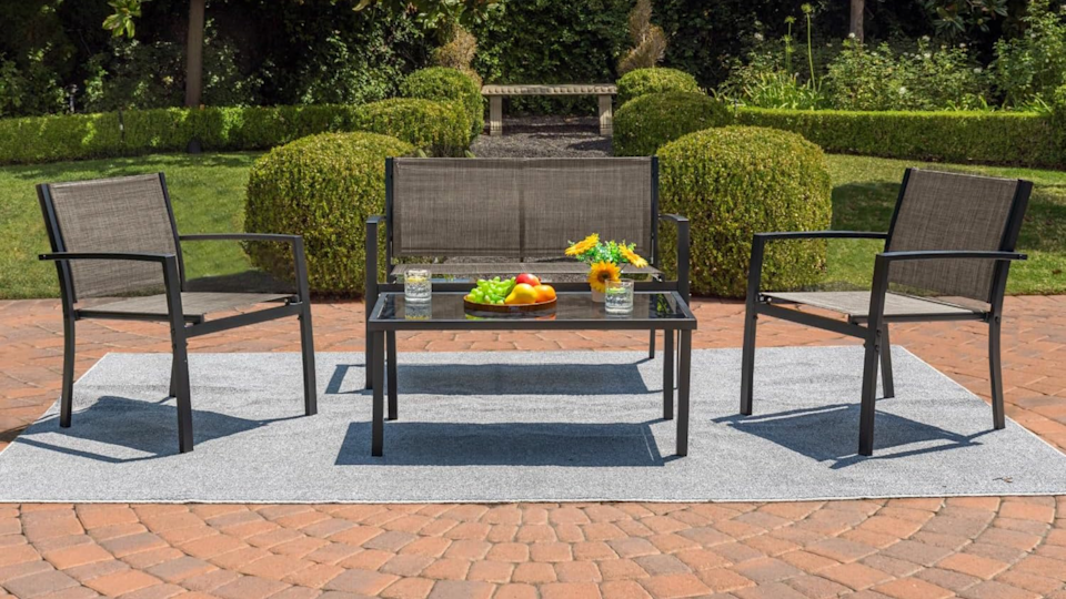 The 4-piece patio set on an outdoor patio, with fruit, flowers and drinking glasses on the coffee table