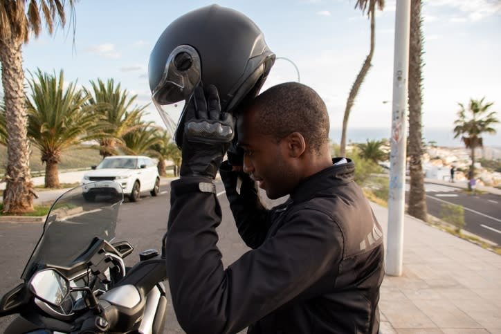 A person in motorcycle equipment places his helme