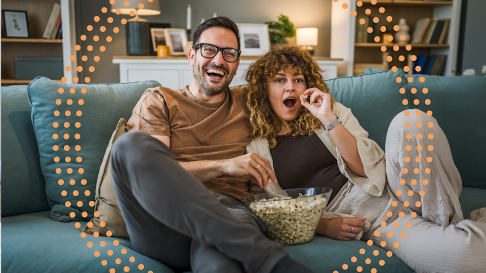 Couple sitting on their couch with popcorn watching TV. 