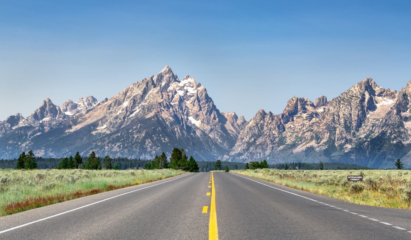 Open road on a sunny day in Wyoming, USA, with mountains in the background