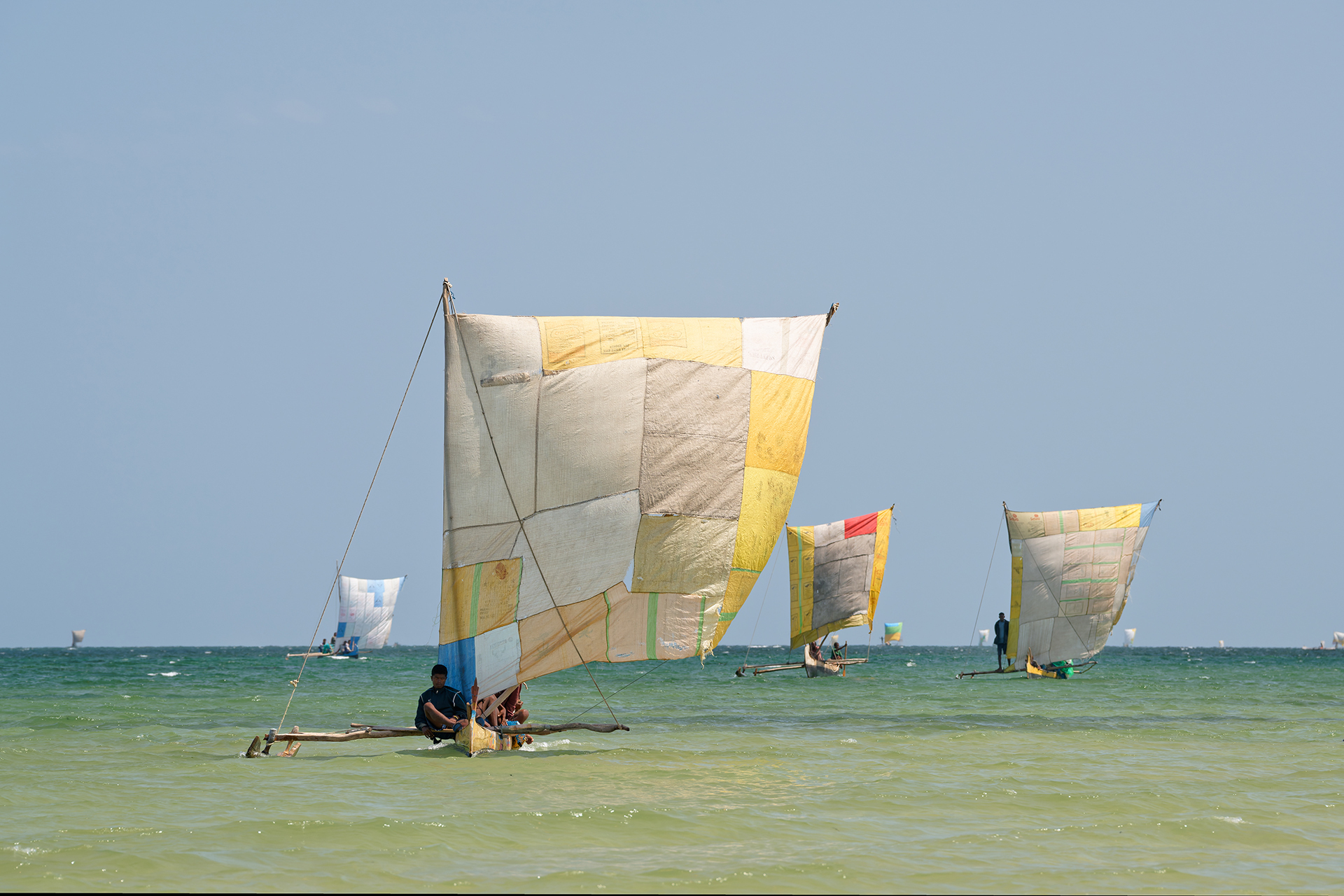 Malagasy fishermen sail in shallow waters with colorful-sailed pirogues.