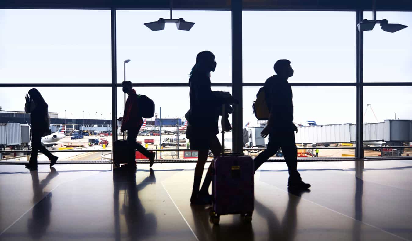 People silhouette next to a window at the airport as they walk to their gate